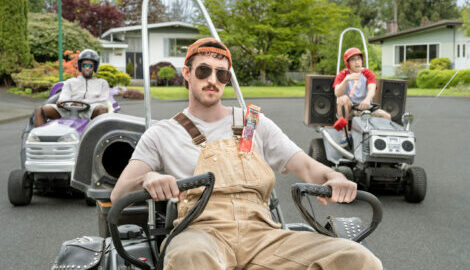 Three guys riding in go-karts around their suburban neighborhood, with visible beef sticks in their pocket.