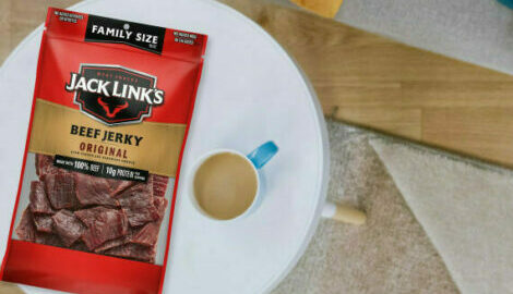 A family sized bag of jerky next to a cup of coffee on a coffee table.