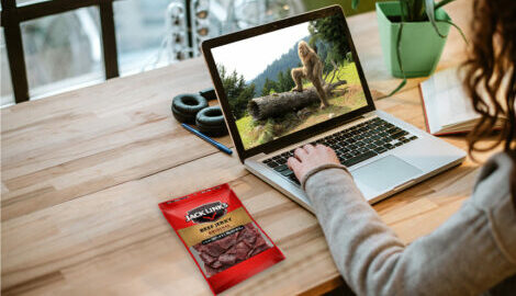 Woman working from home with a bag of Jack Links Original Beef jerky next to her.