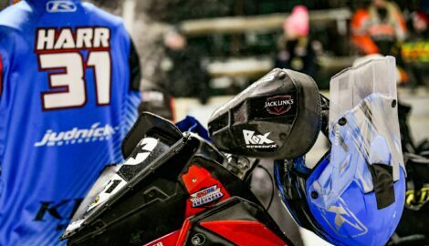 From left to right: The back of racer Emil Harr's jacket visible alongside his snowmobile, sponsored by Jack Link's.
